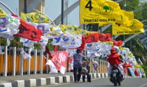 Pedagang mendorong gerobak berisi buah melintas di depan sejumlah bendera partai politik nasional yang dipasang di jembatan Pantee Pirak, Kota Banda Aceh, Sabtu (23/3/2026). ilustrasi parpol